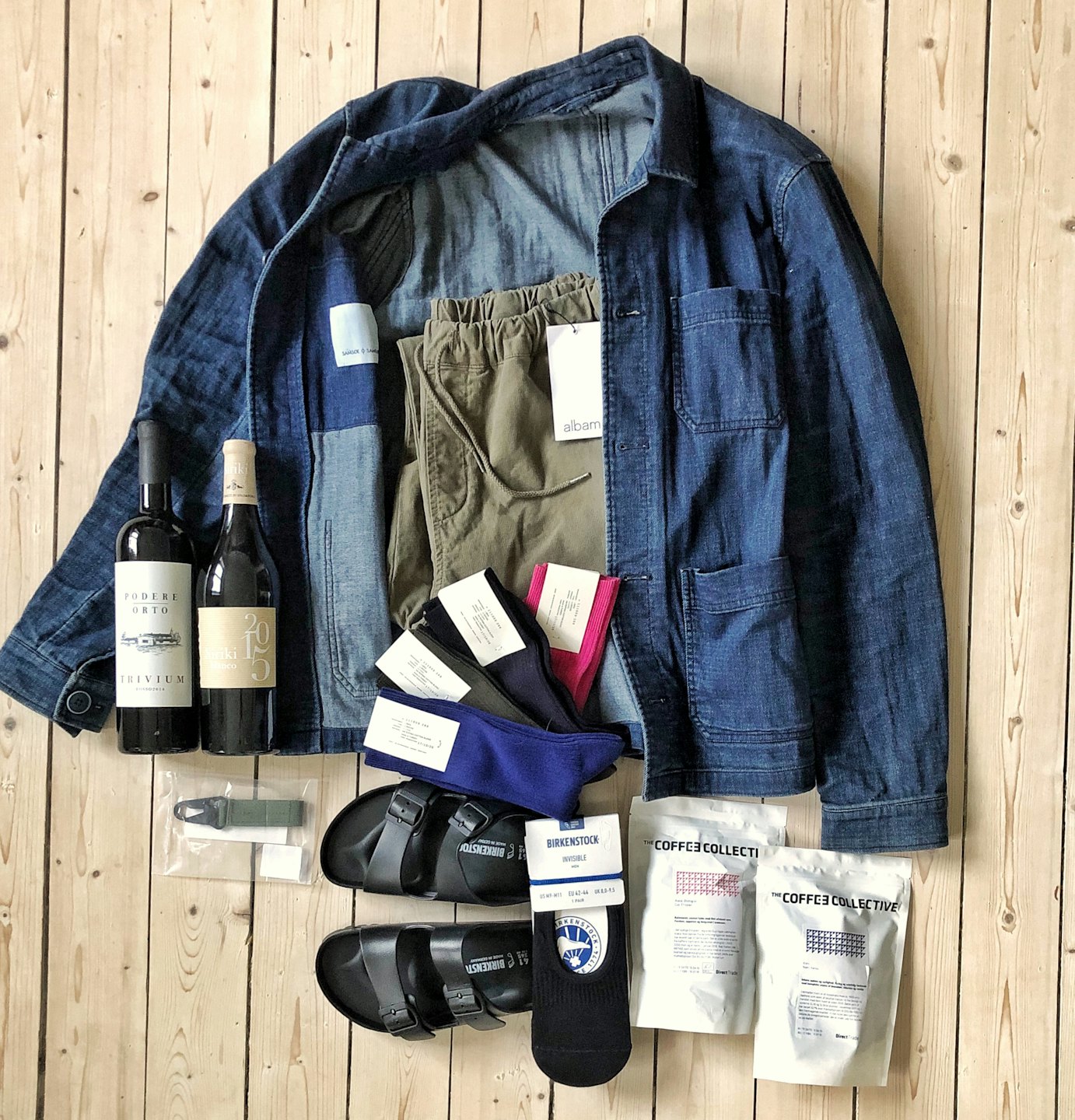 Home Denim jacket, pants, socks, and wine laid out on wood floor.